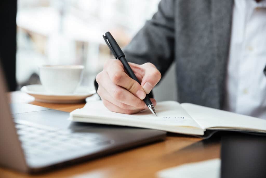An image of a businessman sitting at a table in a cafe, working on a laptop. This image conveys a professional and productive atmosphere, highlighting the practical applications of The Match Guy services.