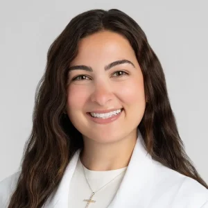 Heya Batah, in a medical coat, smiling confidently. Internal Medicine Resident at The Cleveland Clinic.
